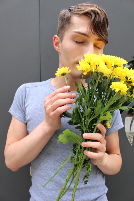 Mister Matthew trägt ein graues T-Shirt und riecht an gelben Blumen